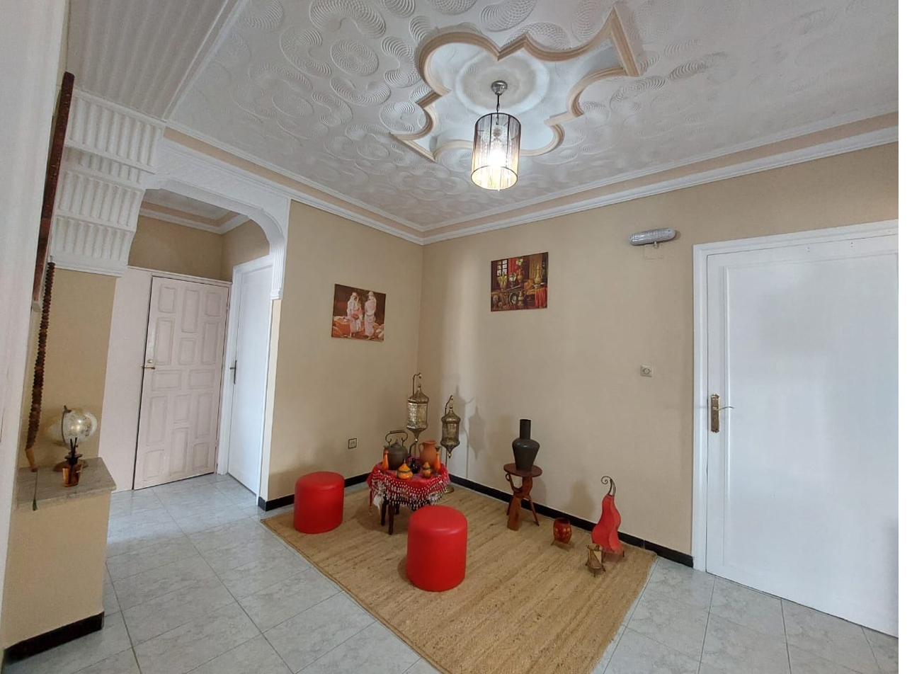 Hall d'entrée de Dar Kamilia avec arche mauresque, lanternes en laiton et pouf rouge terracotta