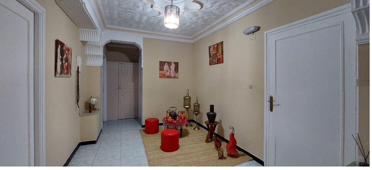 Hall central de Dar Kamilia : plafond travaillé, lanterne suspendue, peintures encadrées et pouf rouge