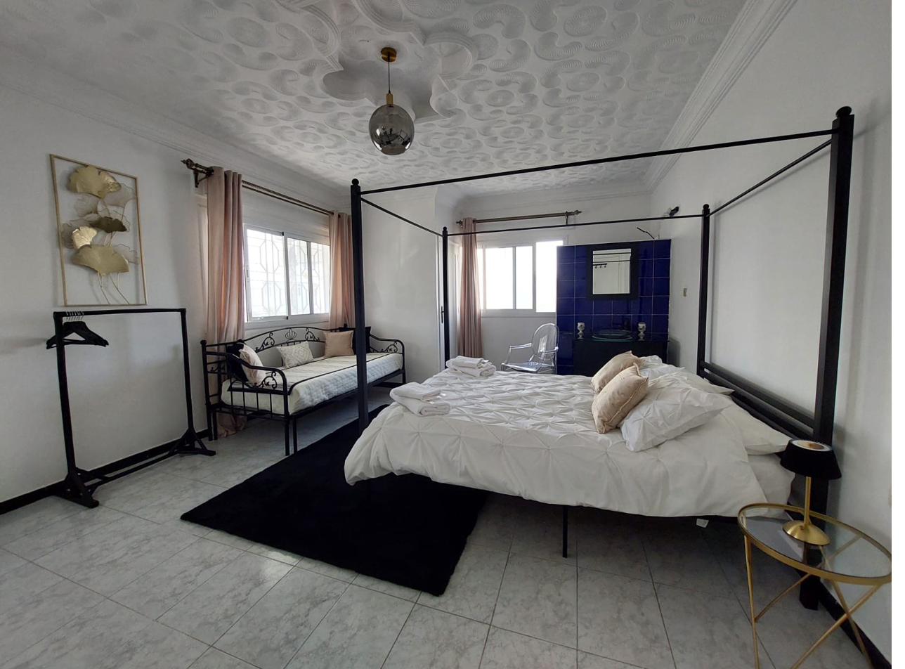 Suite Kamilia : grande chambre lumineuse avec lit à baldaquin noir et coin salon