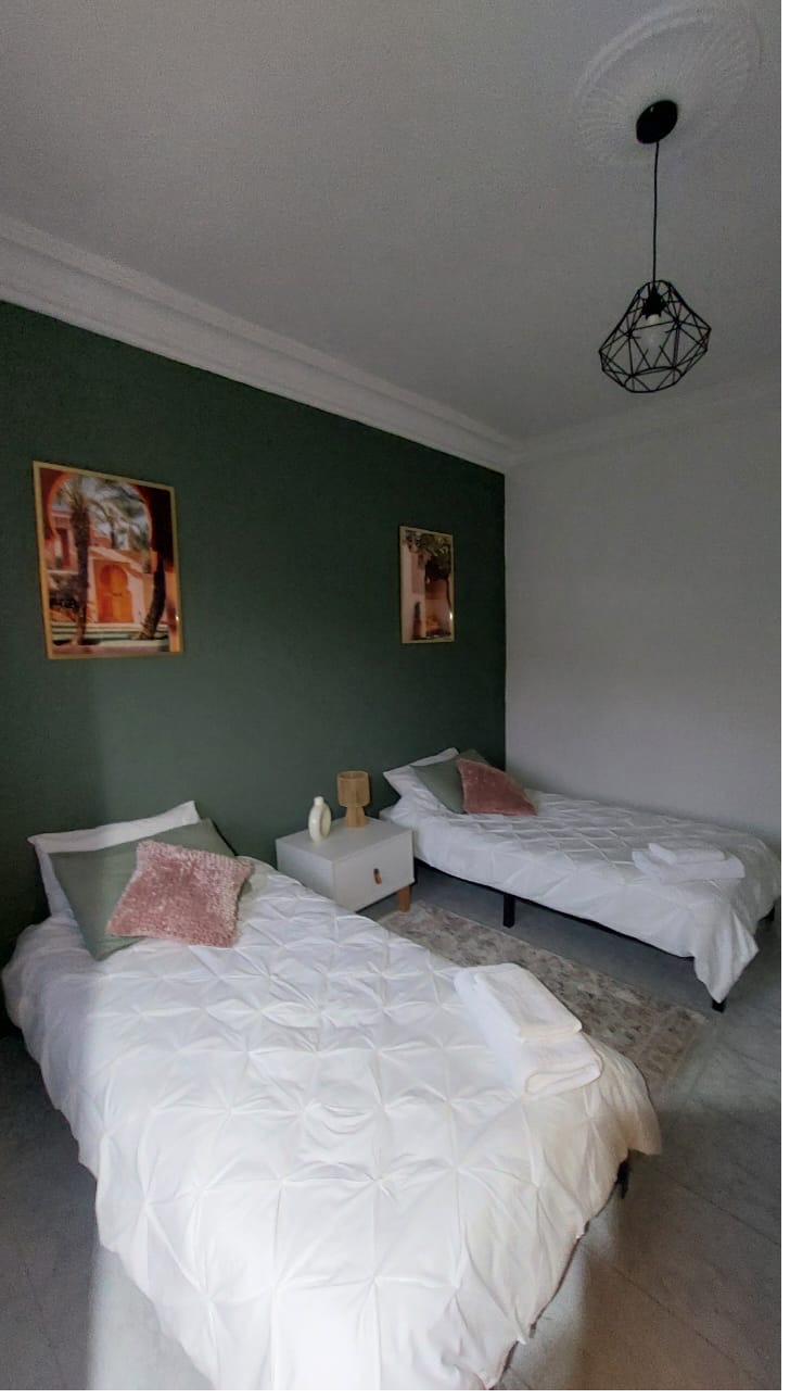 Chambre Malik : mur vert sauge, deux lits simples avec coussins roses poudrés