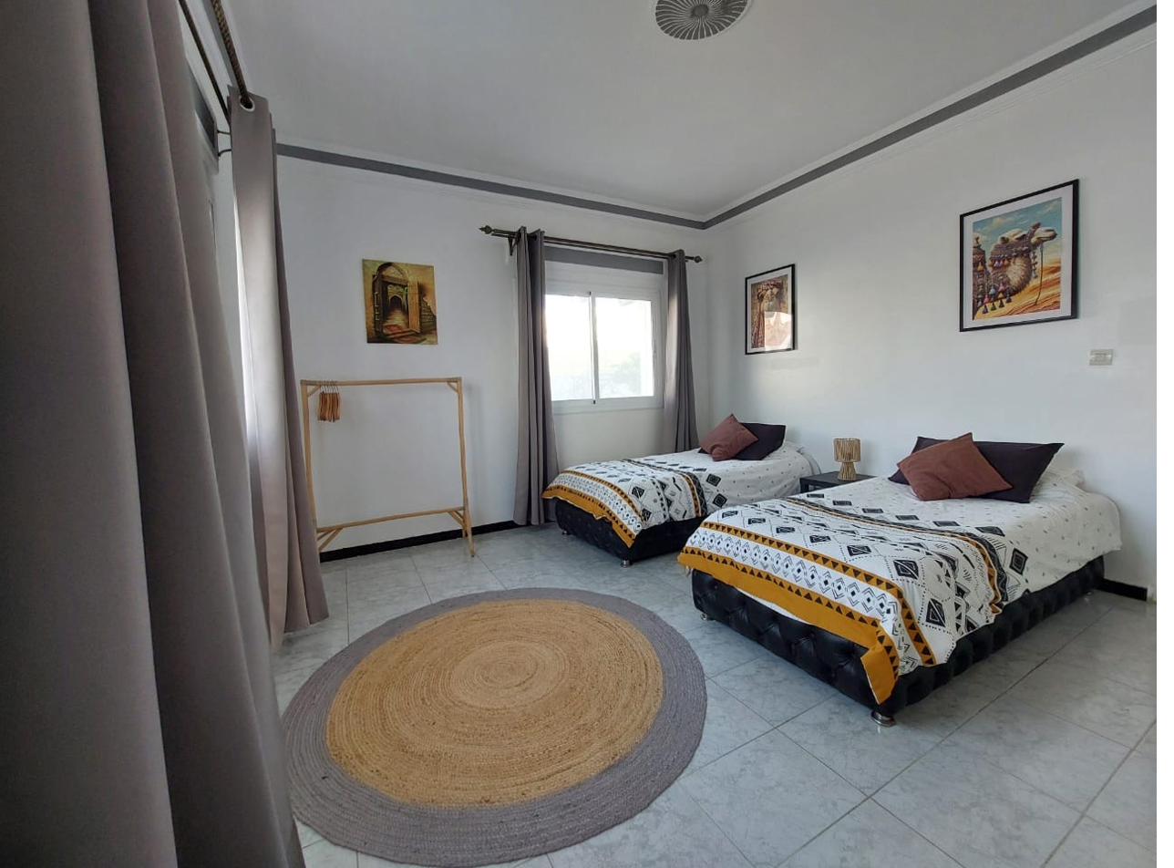 Chambre Maydine : deux lits avec parures graphiques, tapis rond en jute, lumière naturelle